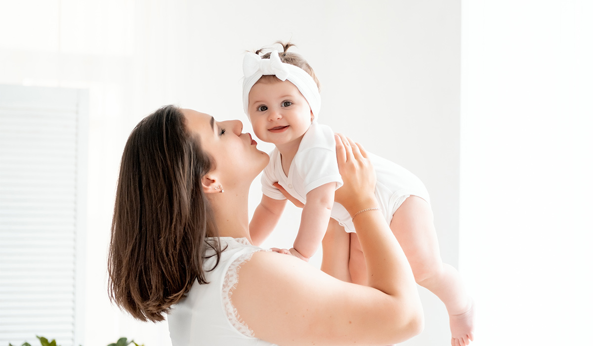 A mother with a small child or infant is playing at home by the window in the children's room. Happy maternity leave, mom's love and care, space for text.; Shutterstock ID 2502364003; purchase_order: -; job: -; client: -; other: