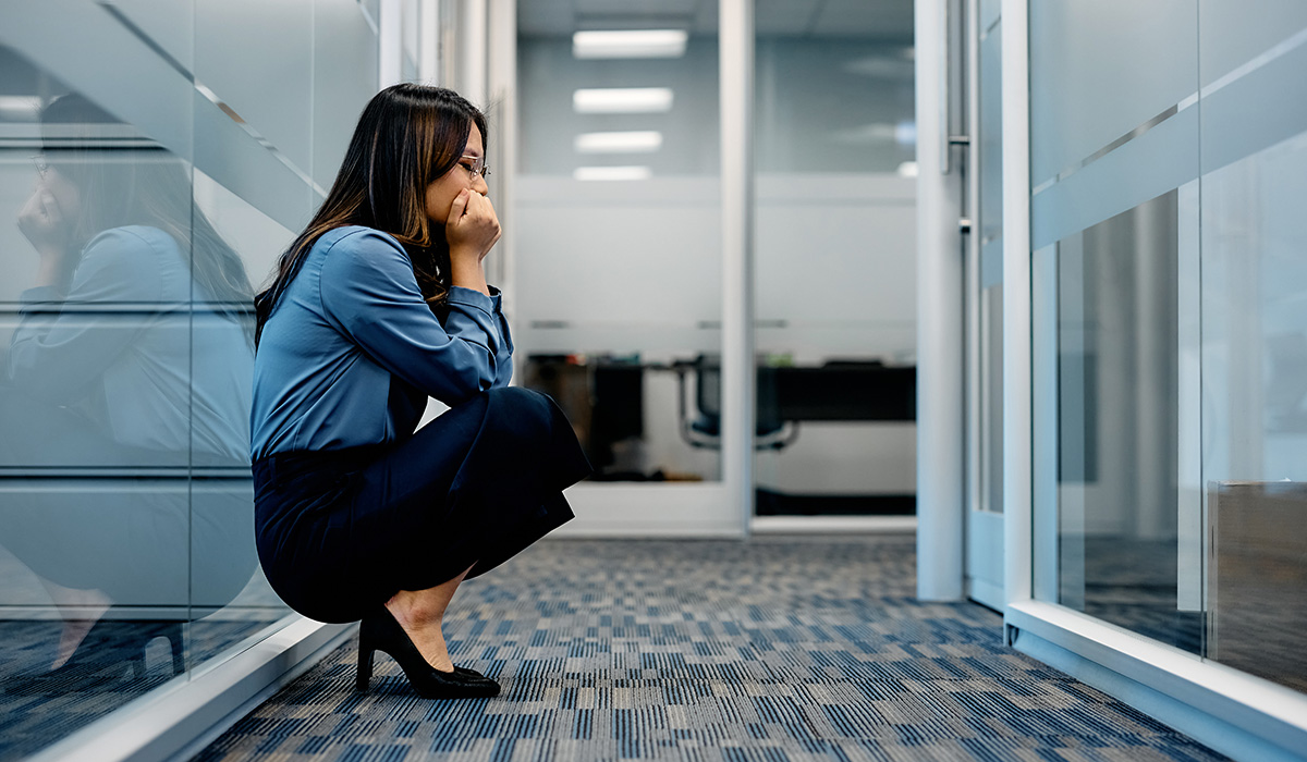Stressed out Asian businesswoman crouching in hallway on an office building. Copy space.