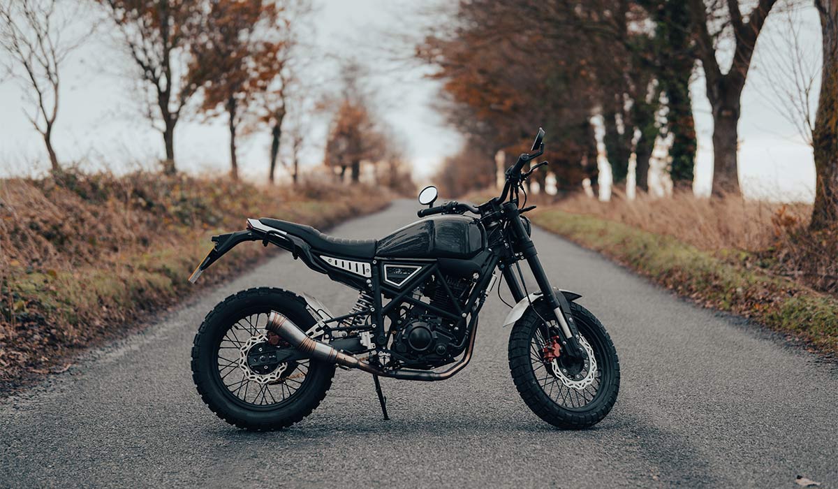 Scrambler motorcycle off-road machine, motorbike parked on a forest road with autumn trees and leaves; Shutterstock ID 2268600057; purchase_order: -; job: -; client: -; other: