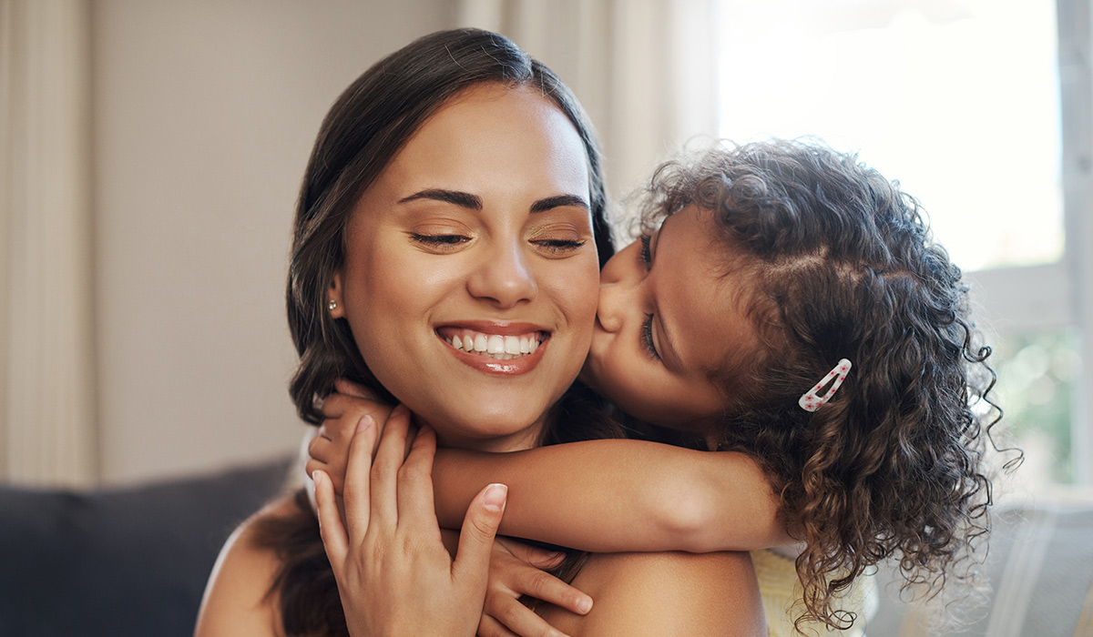 Mom, daughter and hug with kiss on sofa for bonding with love, affection and childhood security for support. Mother, girl and relax with care in living room of home, together and nurture connection.; Shutterstock ID 2478229011; purchase_order: -; job: -; client: -; other: