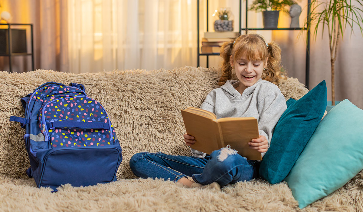 Young teenager girl taking a fairy tale book from backpack at home, flipping reading pages with interest. Blonde child kid on sofa pauses to admire illustrations, grinning at each charming scene.; Shutterstock ID 2659147695; purchase_order: -; job: -; client: -; other: