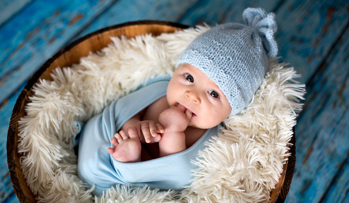 Little baby boy with knitted hat in a basket, happily smiling and looking at camera, isolated studio shot; Shutterstock ID 765918223; purchase_order: -; job: -; client: -; other: