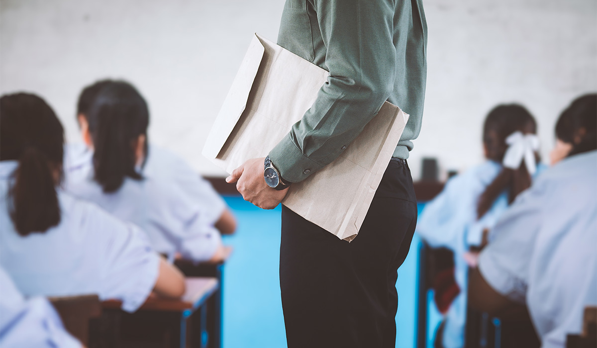The teacher holds the exam paper and controls the exam room while the students sit and take the exam with stress; Shutterstock ID 2522526917; purchase_order: -; job: -; client: -; other: