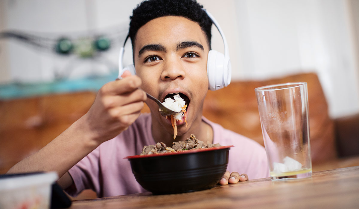 Portrait teenage boy with headphones eating at coffee table