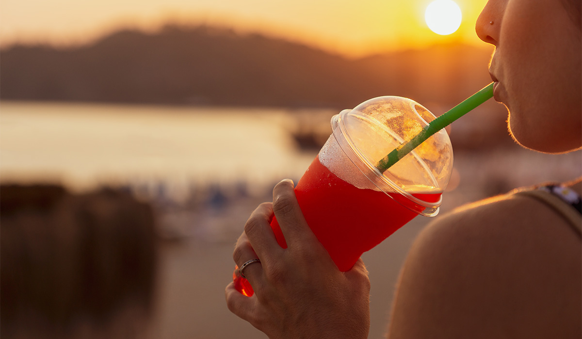 Unrecognizable young woman in the foreground enjoying a slushy at sunset while drinking through a straw.; Shutterstock ID 2223931749; purchase_order: -; job: -; client: -; other: