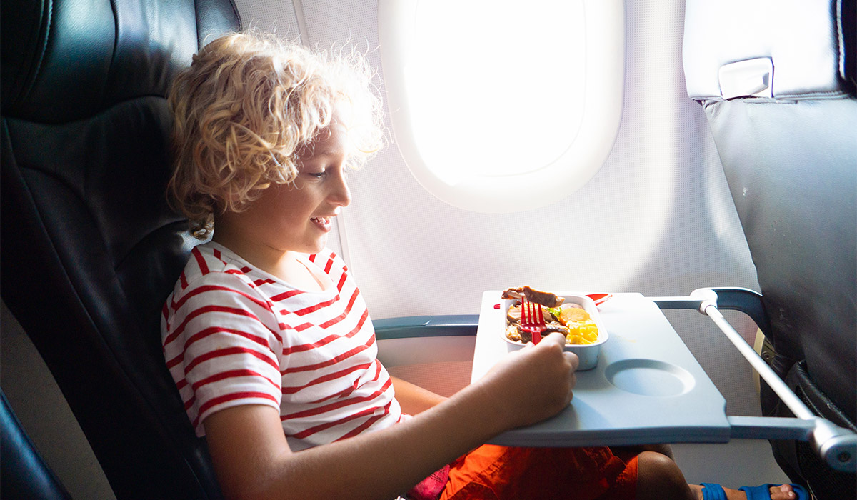 Child in airplane window seat. Kids flight meal. Children fly. Special inflight menu, food and drink for baby and kid. Boy eating healthy lunch in airplane. Travel and family vacation. ; Shutterstock ID 2366718833; purchase_order: -; job: -; client: -; other: