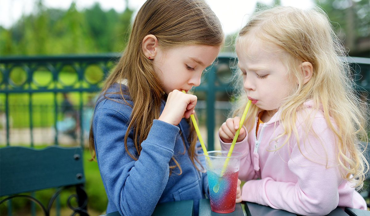 Two cute little sisters drinking colorful frozen slushie drink on hot summer day; Shutterstock ID 530498494; purchase_order: -; job: -; client: -; other: