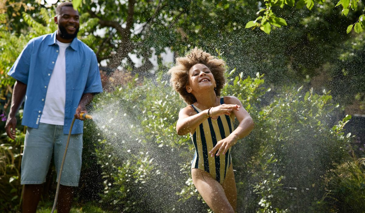 Father spraying child with garden hose