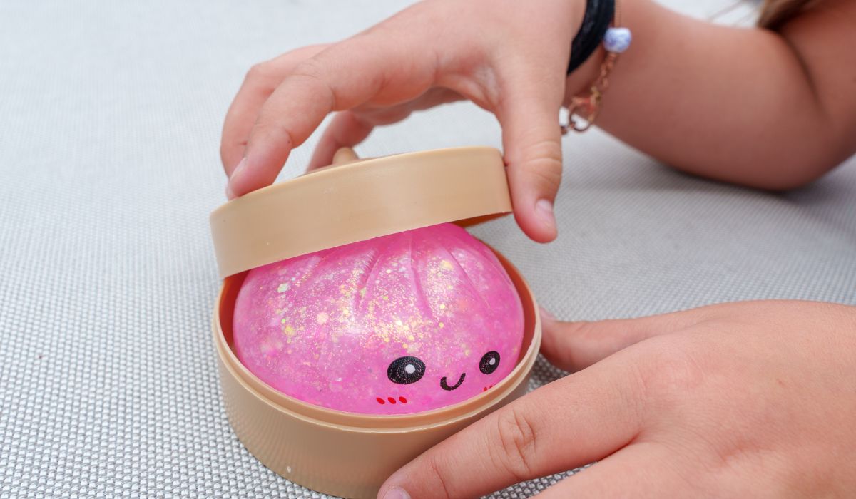 Child's hands open a container holding a cute pink dumpling-shaped squishy toy